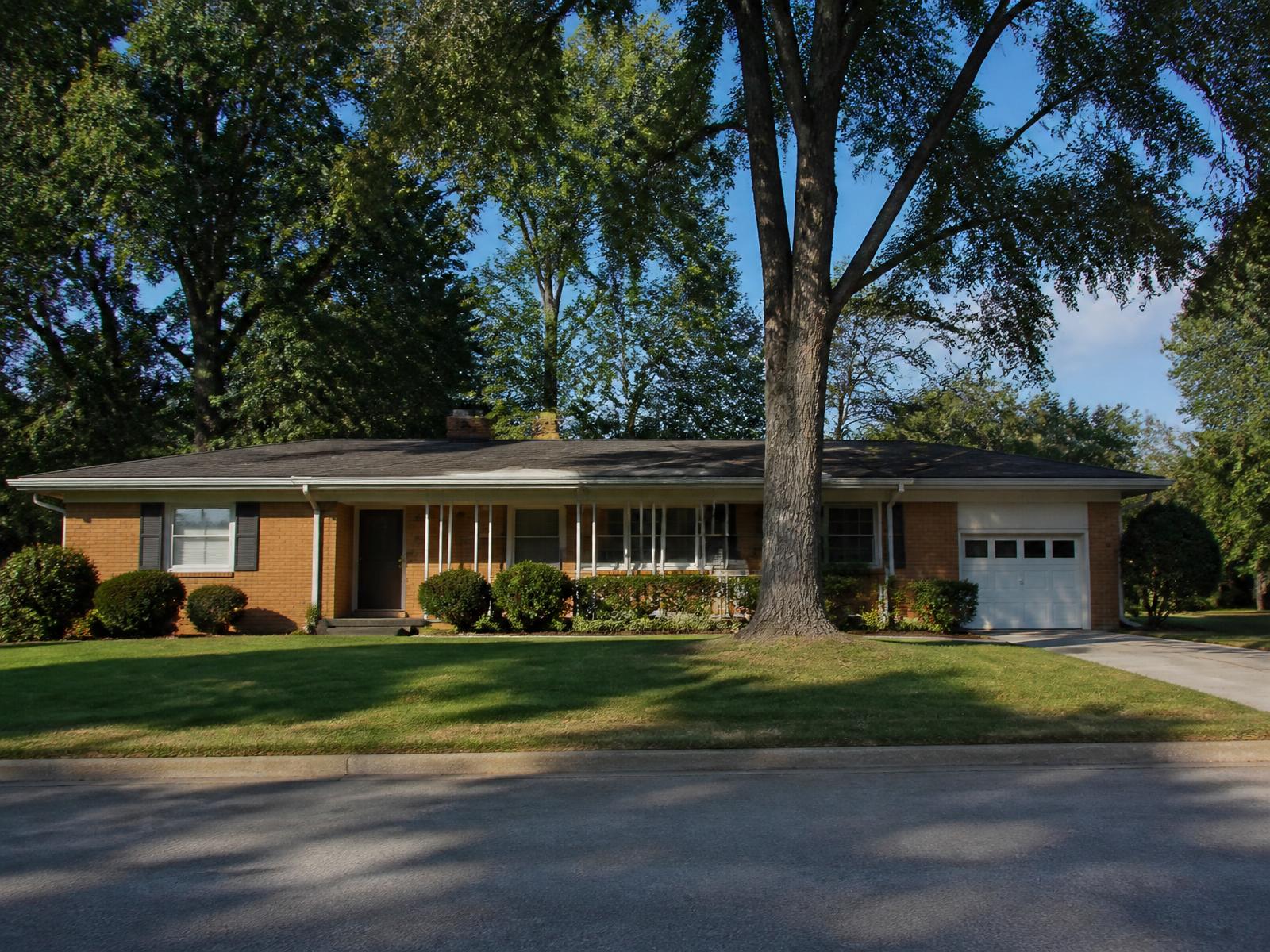 Low-slung mid-century brick ranch home with mature shade trees in a postwar Charlotte neighborhood