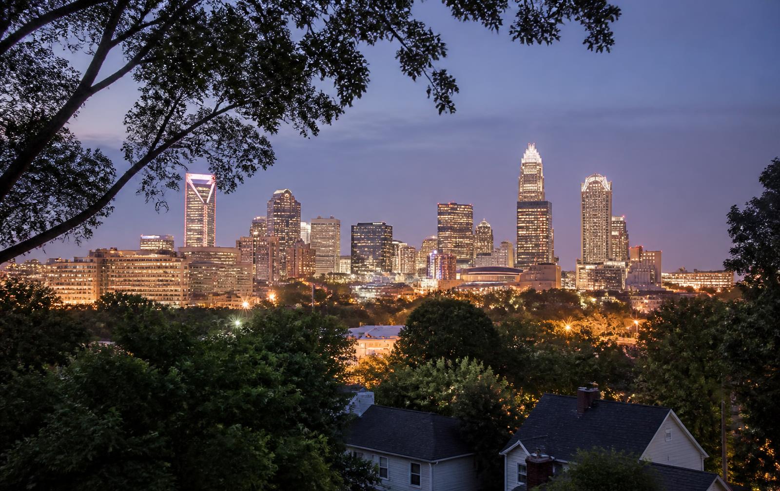 The Charlotte skyline at dusk seen from a leafy residential ridge